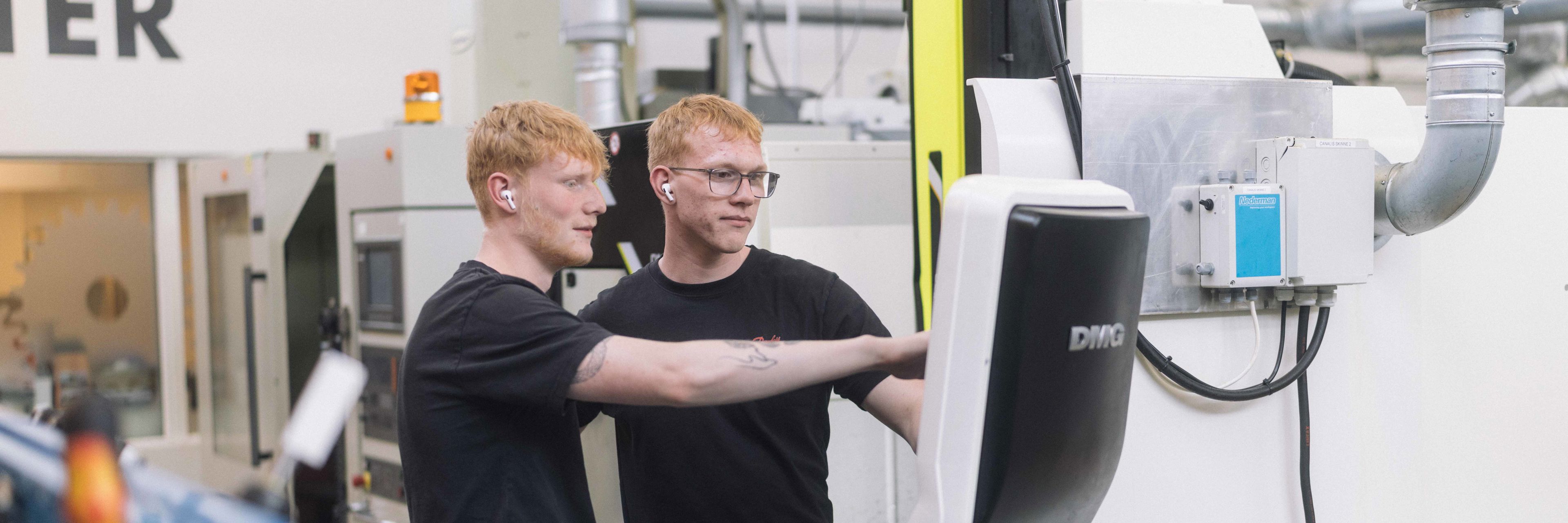 To unge mænd står og kigger på en skærm foran en stor maksine.