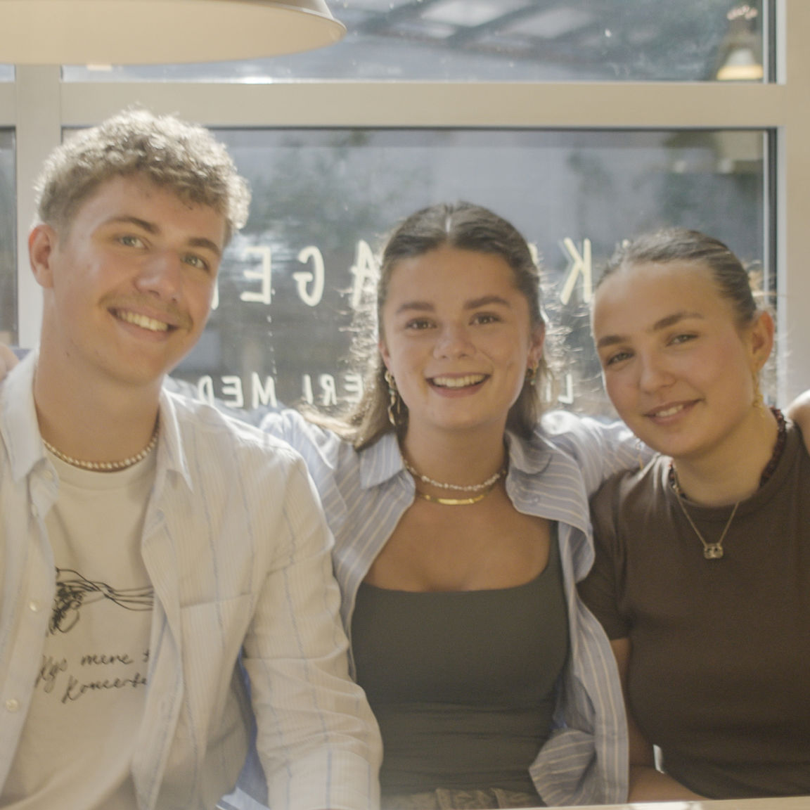 Tre unge studerende sidder sammen og smiler til kameraet.