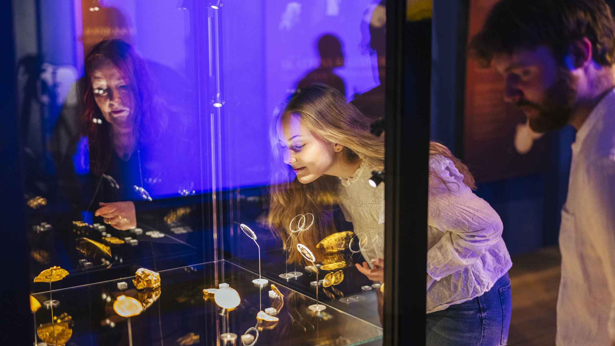 to kvinder og en mand står og kigger på en udstilling i en montre.