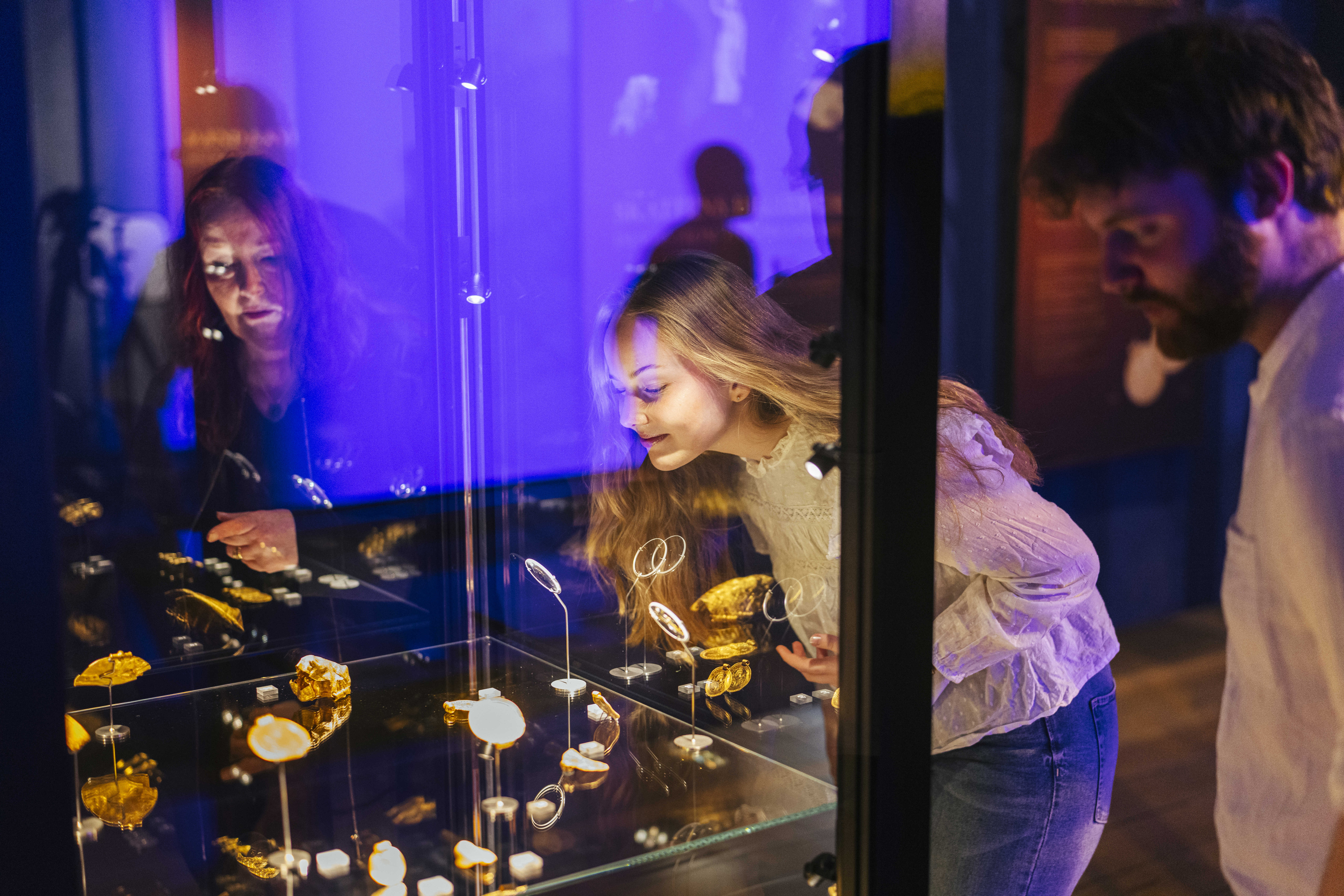 to kvinder og en mand står og kigger på en udstilling i en montre.