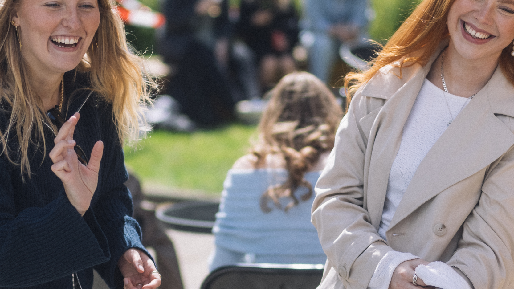 To kvinder står udenfor og griner, ser væk fra kameraet.