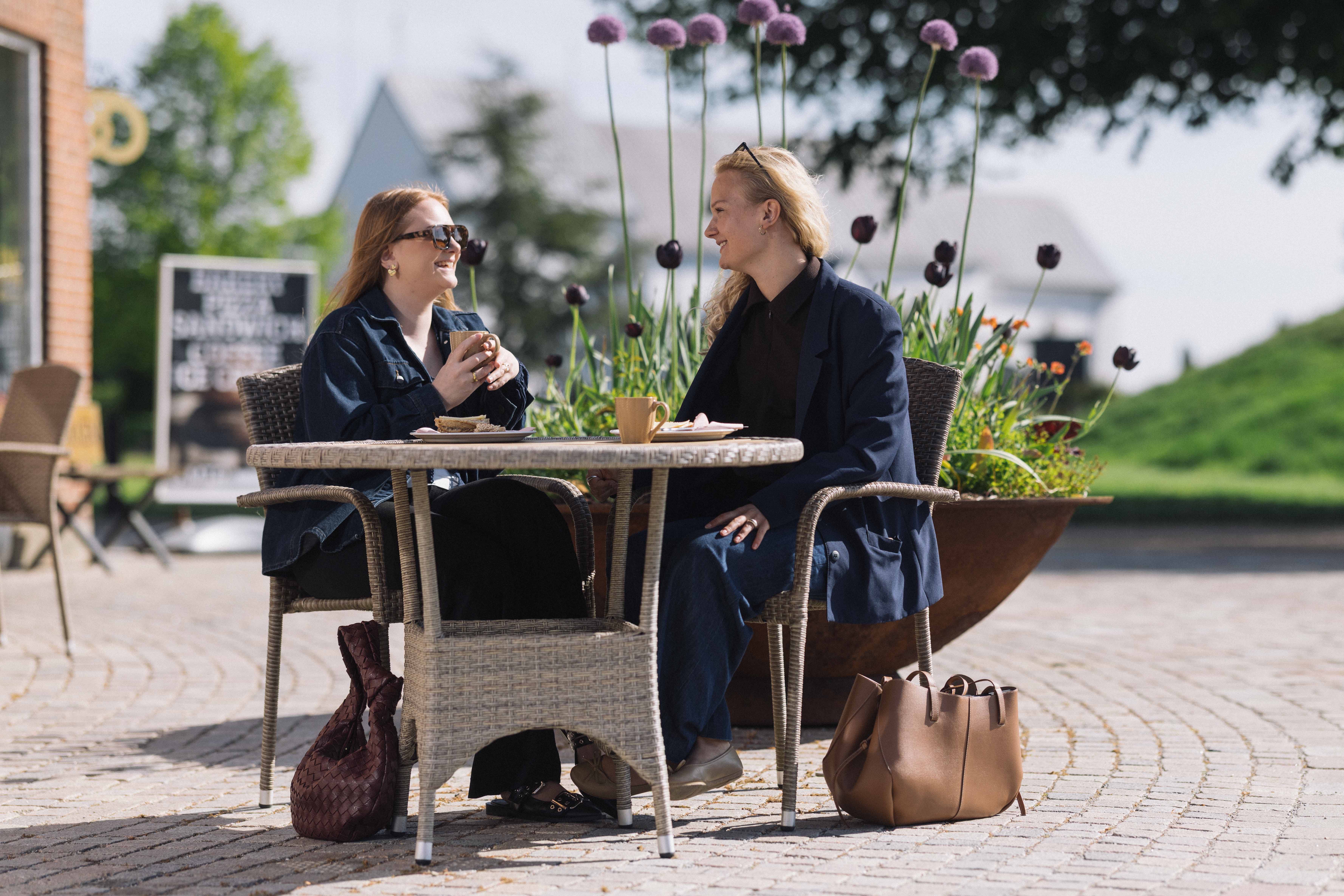 To kvinder sidder ved et bord, drikker kaffe og snakker.